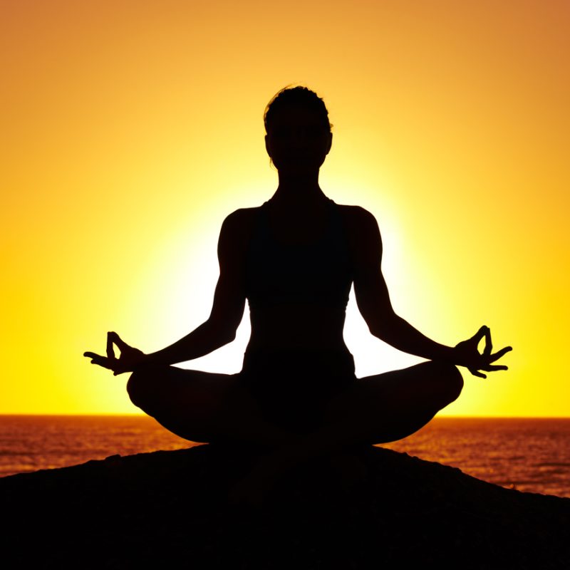 Silhouette of a woman doing yoga on the beach at sunset