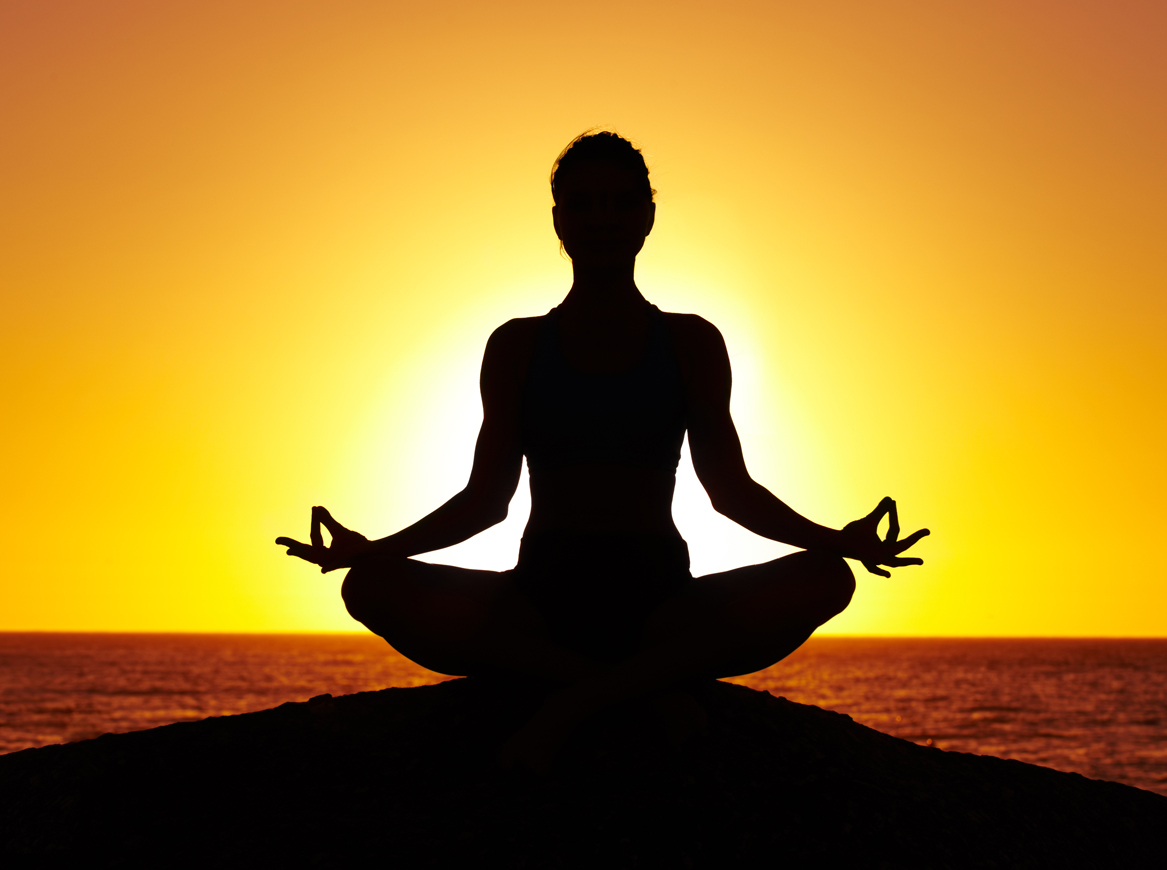 Silhouette of a woman doing yoga on the beach at sunset